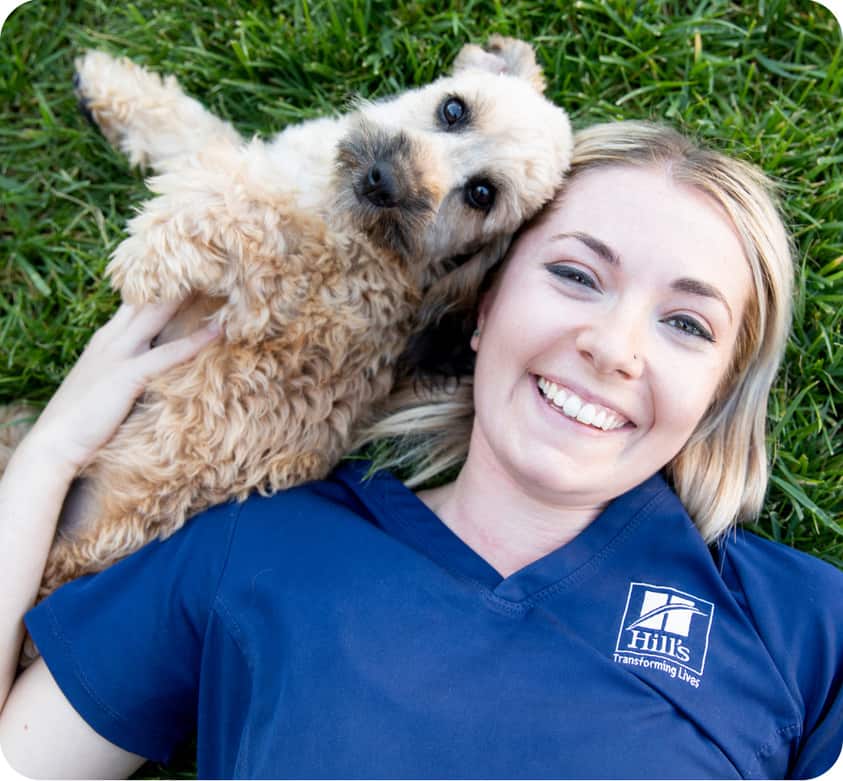 A small dog lying in the grass next to a Hill's researcher